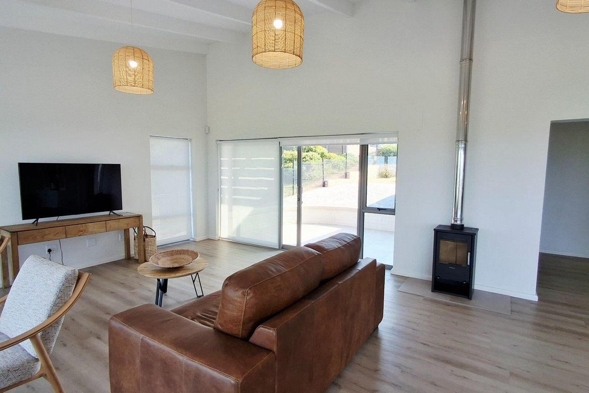 Bright living room featuring high ceilings with exposed beams, wood-burning fireplace, and large sliding glass doors providing access to the outdoor area.