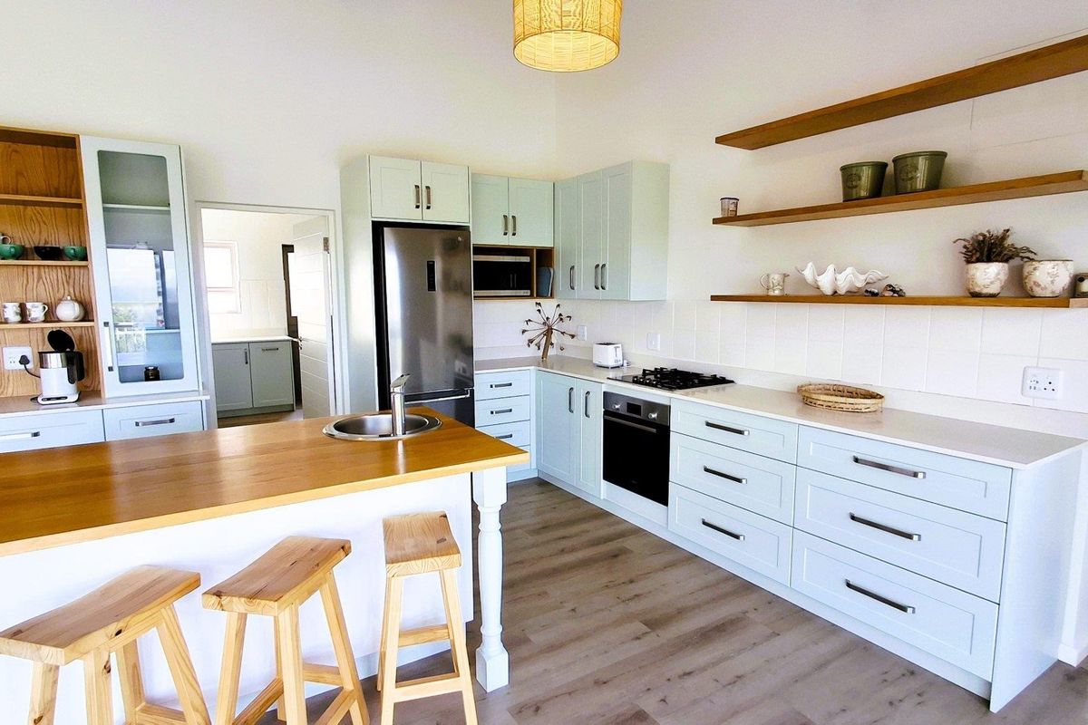 Modern kitchen featuring light-toned shaker cabinetry, timber-topped island with integrated sink, built-in oven, gas hob, and open shelving, finished with durable laminate flooring.