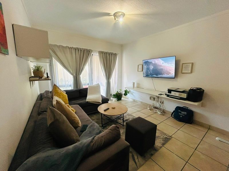 A functional living room featuring ceramic floor tiles, a floating media shelf, and access to a balcony through sliding glass doors.