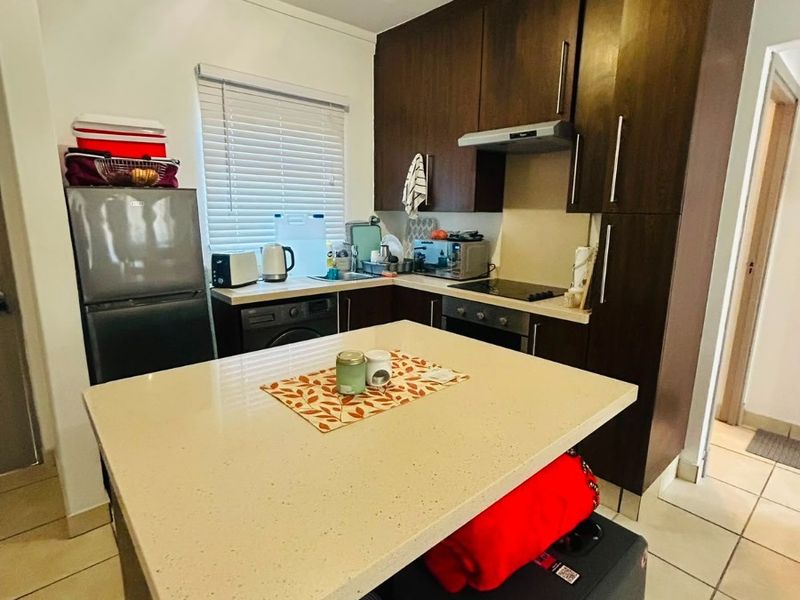 Compact kitchen featuring dark wood cabinetry, stone countertops, built-in oven, hob, and extractor fan, complemented by tiled flooring and natural light.