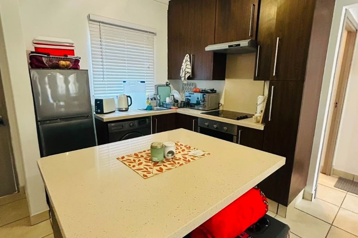 Compact kitchen featuring dark wood cabinetry, stone countertops, built-in oven, hob, and extractor fan, complemented by tiled flooring and natural light.