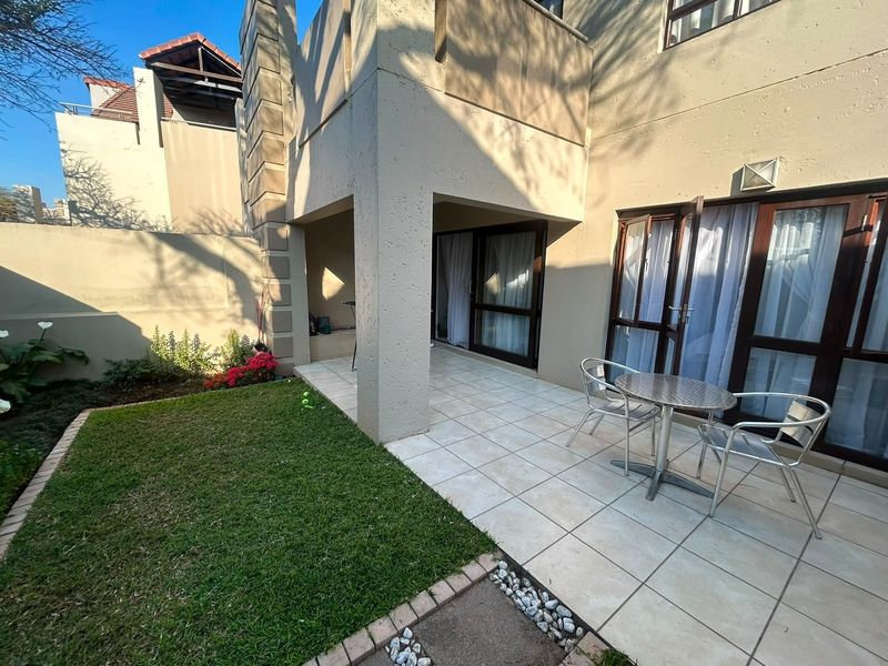 A private rear patio area featuring tiled flooring, direct access to the interior via sliding doors, and a small adjacent lawn.