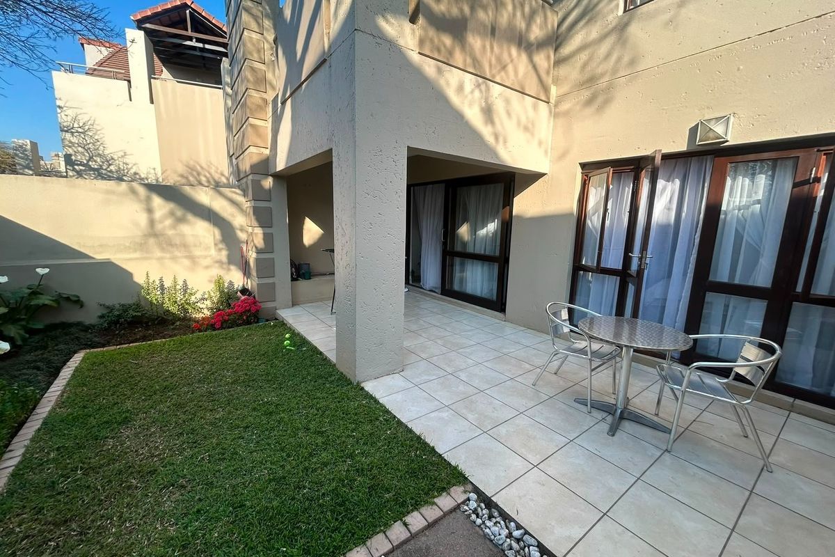 A private rear patio area featuring tiled flooring, direct access to the interior via sliding doors, and a small adjacent lawn.
