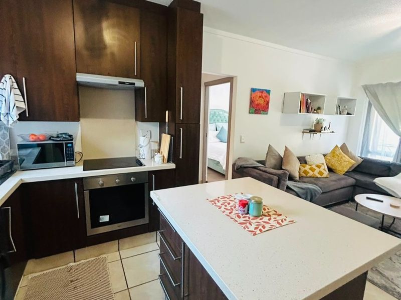 Open-plan kitchen and living area featuring dark wood cabinetry, a central island with stone countertops, and tiled flooring throughout.