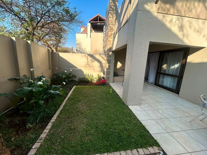A private rear garden featuring a tiled patio area, a small lawn, and a boundary wall, accessible via sliding glass doors.