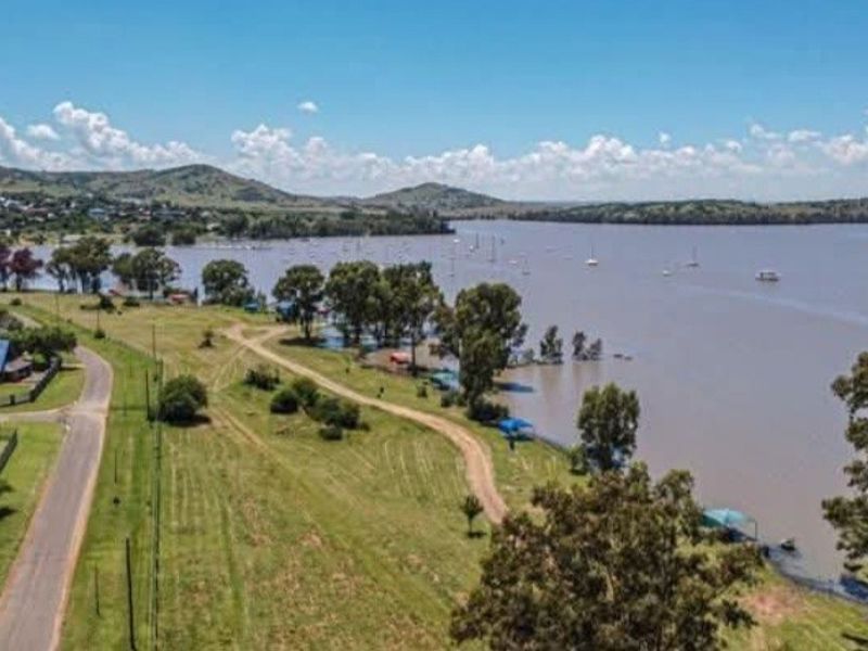 Aerial view of a vacant residential plot featuring direct waterfront access and an unpaved access road, overlooking a large dam or lake.