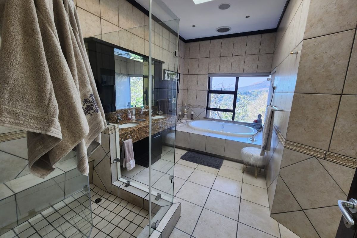 Spacious bathroom featuring a built-in bathtub, glass shower enclosure, dual vanity basins, and a skylight, offering a bright and functional layout.