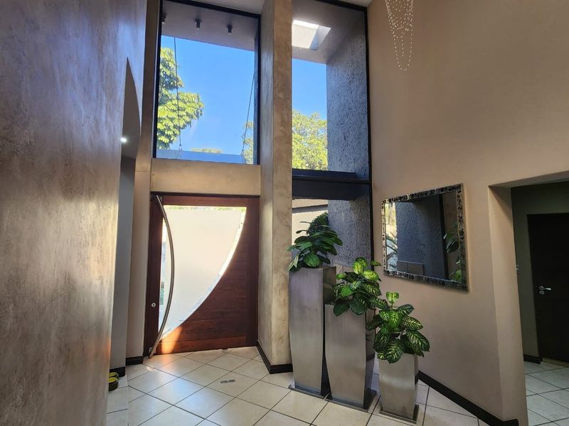 A bright and spacious double-volume entrance hall featuring high ceilings, large windows, and modern textured wall finishes with tiled flooring.