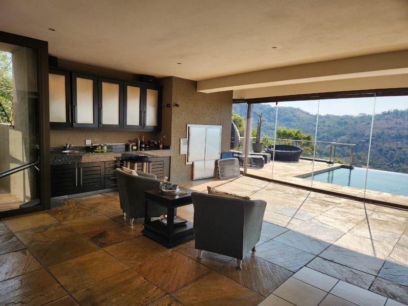 Spacious open-plan entertainment area featuring built-in cabinetry, stone flooring, and seamless stacking glass doors opening to a pool deck with scenic views.