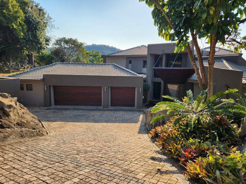 Modern double-story residence featuring a paved driveway, double garage with timber doors, and landscaped rock garden elements.