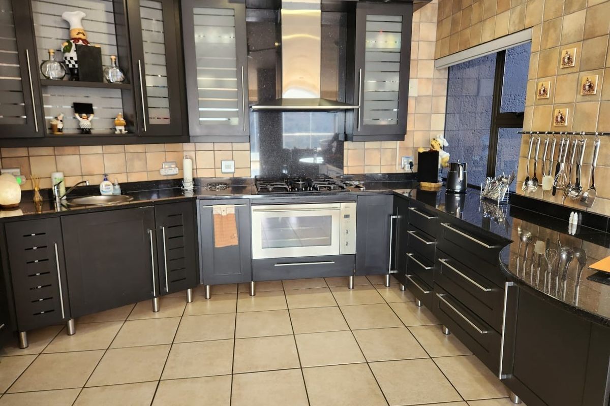 A well-equipped kitchen featuring dark cabinetry, granite countertops, a gas hob, built-in oven, and a stainless steel extractor fan with tiled finishes.