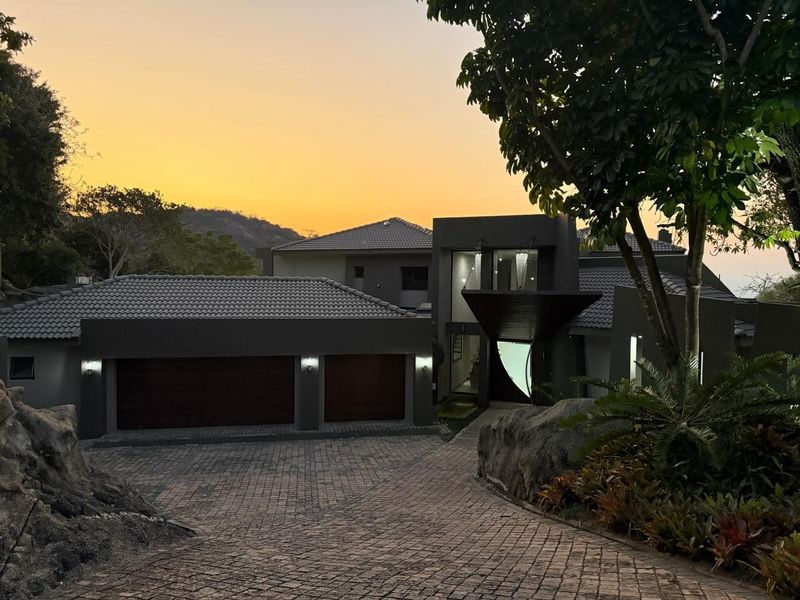 A modern architectural home featuring a double garage, paved driveway, and striking entrance, set against a scenic sunset backdrop.