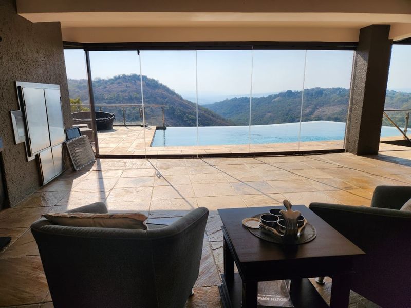 Covered patio featuring stone flooring, built-in braai, and glass stacking doors opening to an infinity pool with expansive mountain views.