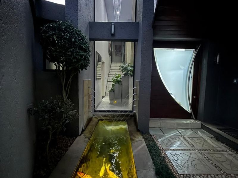 A striking modern entrance featuring a illuminated koi pond water feature, paved walkway, and a contemporary front door leading into a double volume foyer.