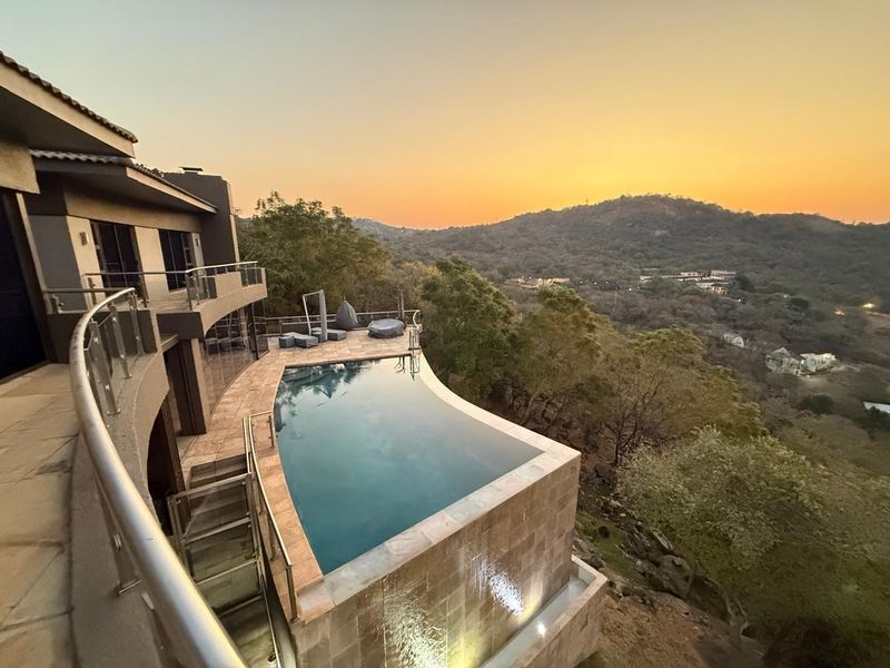 An elevated infinity edge swimming pool with tiled surround and glass balustrades, offering expansive hillside views at sunset.