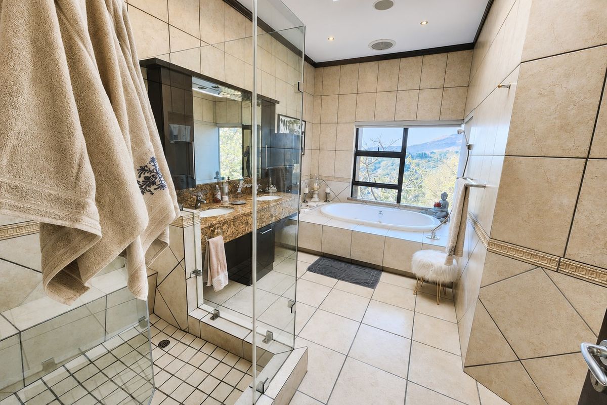 Spacious bathroom featuring a double vanity with granite countertops, a glass-enclosed shower, a built-in bathtub, and a skylight with scenic views.