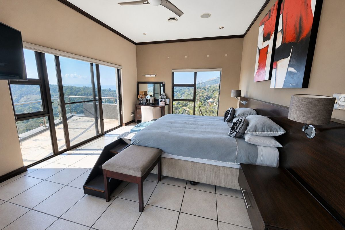 Spacious bedroom featuring tiled flooring, a ceiling fan, and large sliding glass doors opening onto a balcony with scenic views.