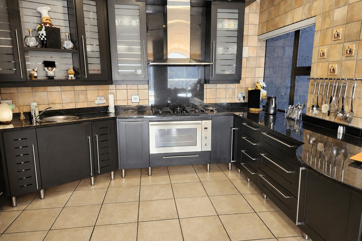 A well-equipped kitchen featuring dark cabinetry, granite countertops, a gas hob, built-in oven, and tiled finishes throughout.