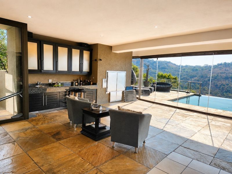Spacious covered patio featuring built-in cabinetry, a sink, and a built-in braai, with seamless glass doors opening to a pool and mountain views.