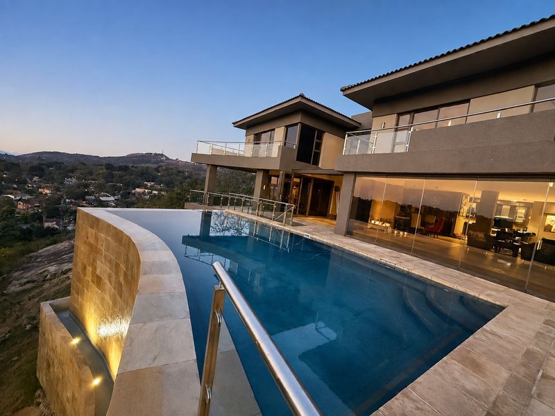 Luxury infinity edge swimming pool with stone cladding and glass balustrades, offering expansive elevated views and seamless indoor-outdoor flow through large glass sliding doors.