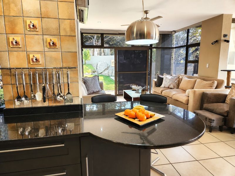 Spacious open-plan living area featuring a modern kitchen with a granite island, tiled floors, and large glass doors leading to the garden.