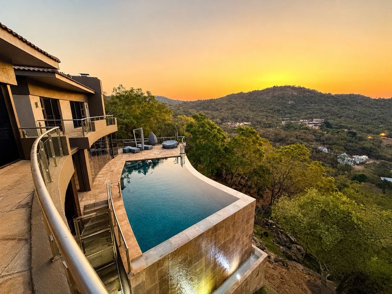 Stunning infinity edge swimming pool with tiled surround and glass balustrades, offering panoramic hillside views at sunset.