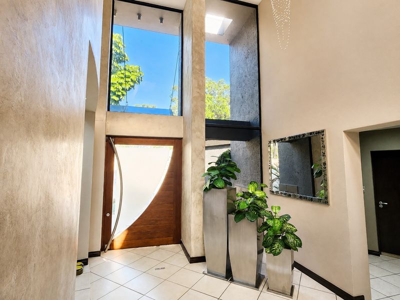 Spacious double-volume entrance hall featuring high ceilings, large floor-to-ceiling windows, and a modern timber pivot front door with tiled flooring.