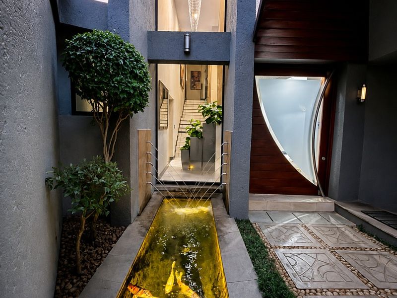 Stunning modern entrance featuring a illuminated koi pond water feature, custom architectural front door, and a double-volume foyer with a grand staircase.
