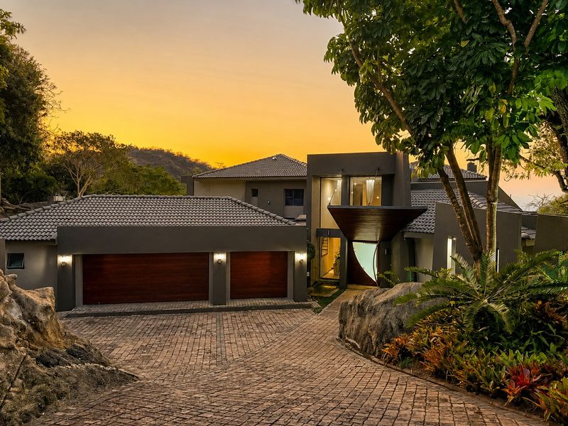 Modern architectural home featuring a double garage, paved driveway, and a striking covered entrance, set against a scenic landscape at sunset.