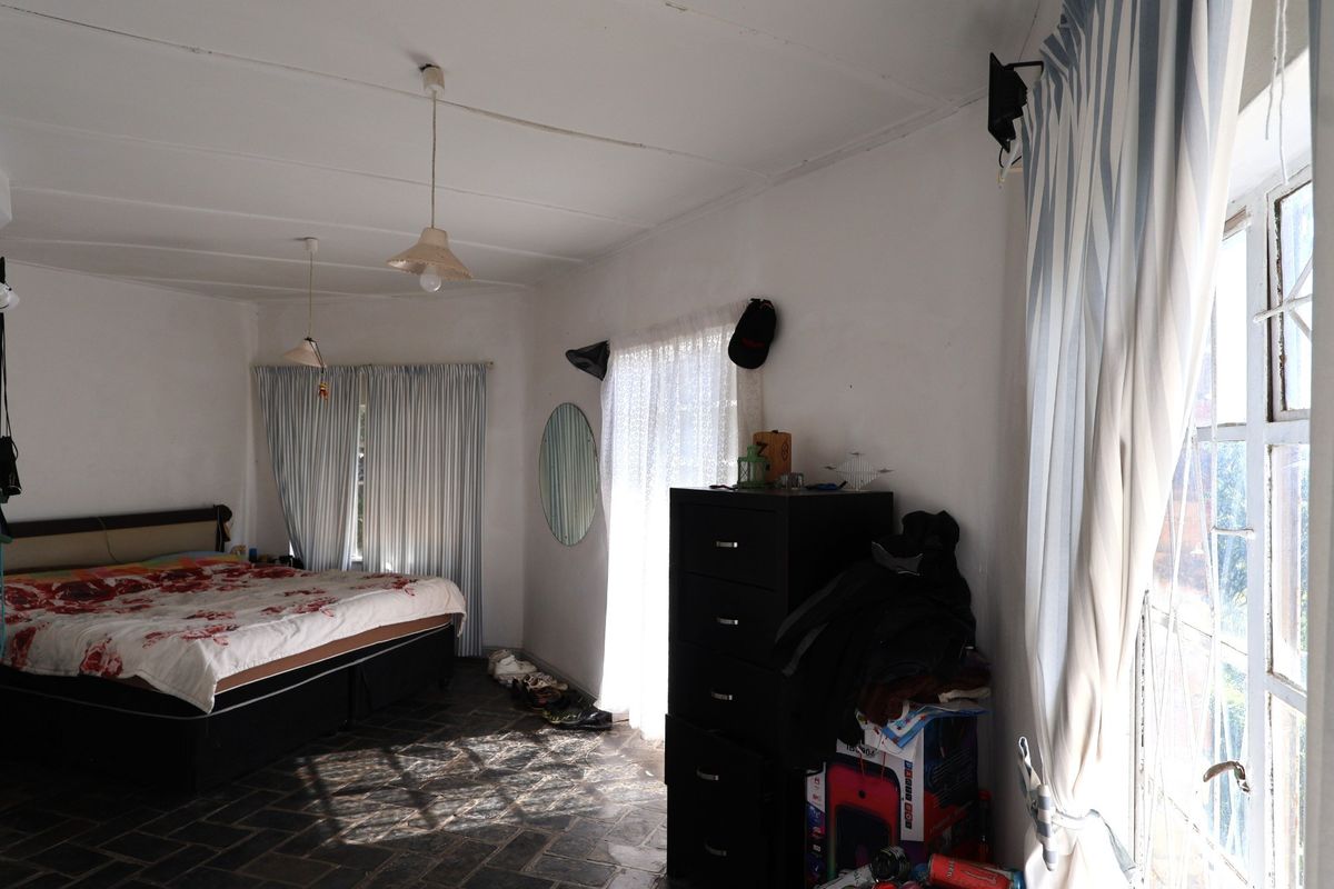A spacious bedroom featuring tiled flooring and multiple windows with curtain rails, offering natural light and potential for cosmetic updates.