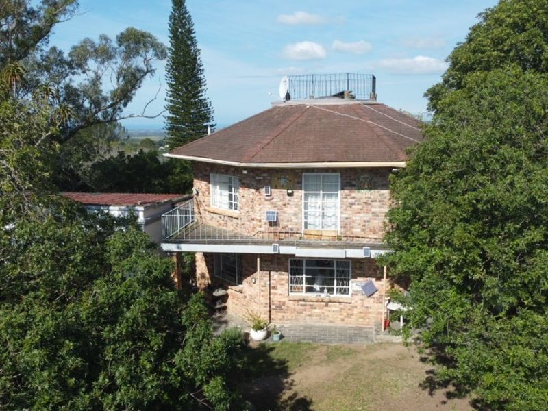 Aerial view of a two-story brick house featuring a tiled roof, balcony with metal railing, and established surrounding trees.