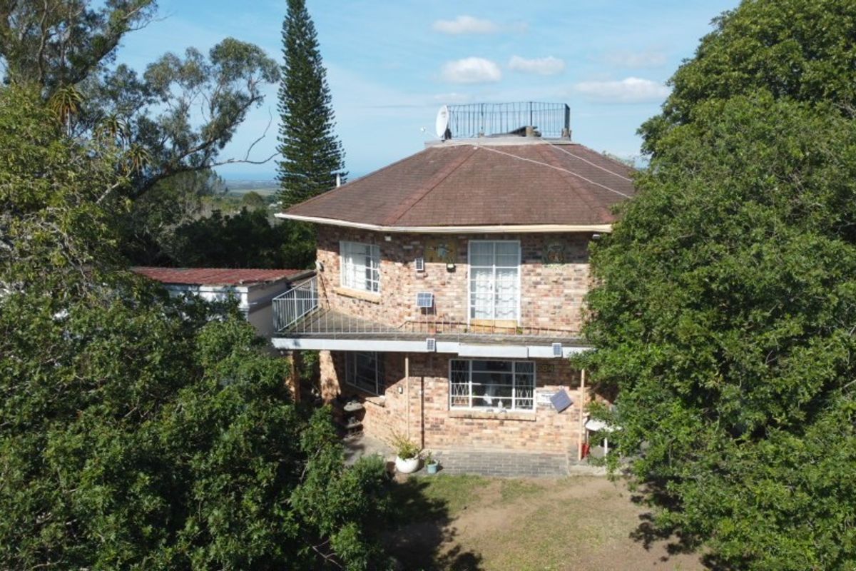 Aerial view of a two-story brick house featuring a tiled roof, balcony with metal railing, and established surrounding trees.