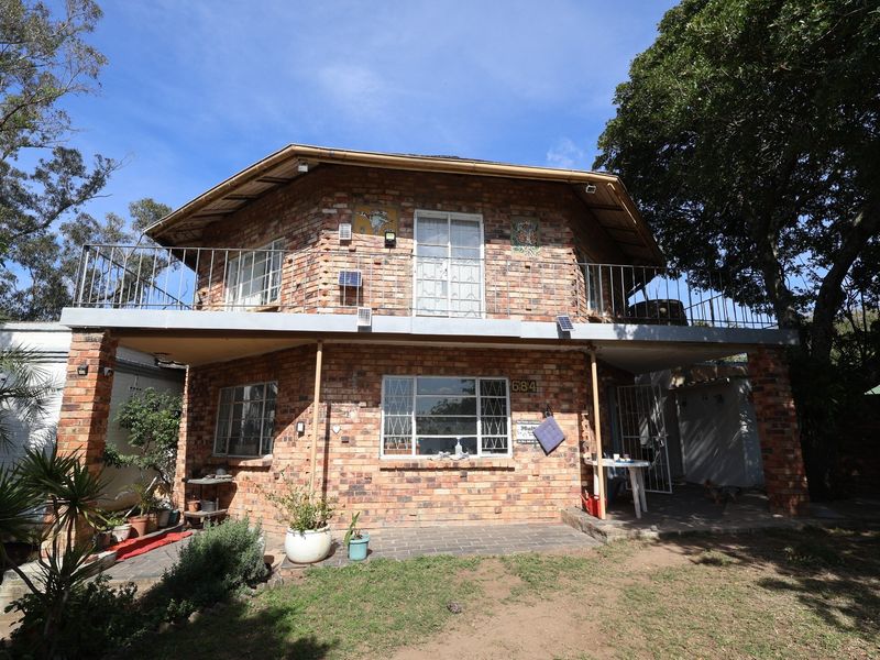 A two-story face-brick house featuring a wrap-around balcony with metal railings, security bars on windows, and a paved ground-level patio area.