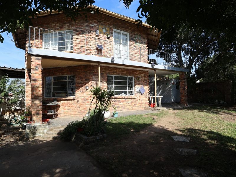 Rear view of a two-story exposed brick house featuring a covered patio, upper-level balcony with metal railings, and a garden area.