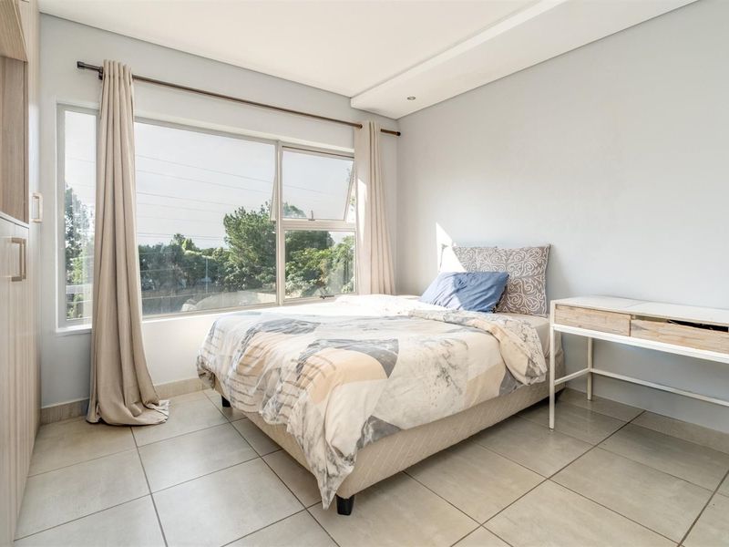 A bright and modern bedroom featuring neutral tiled flooring, built-in cupboards, and a large window with natural light.