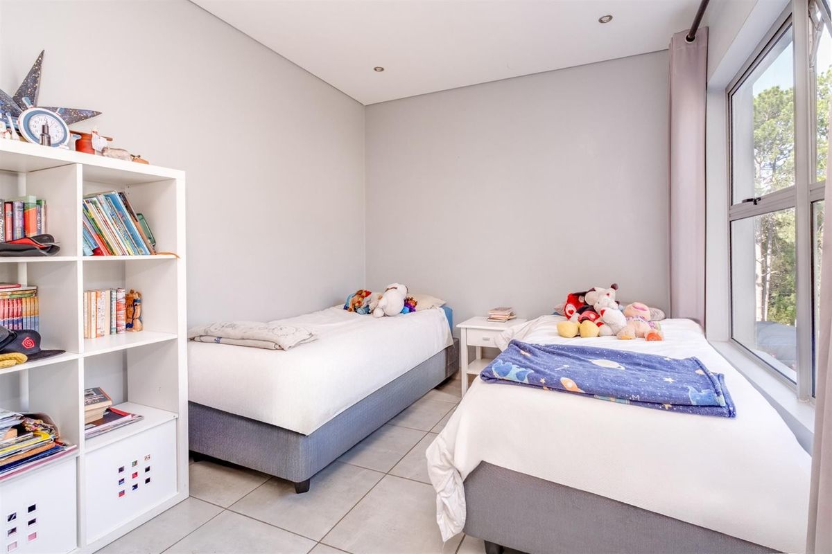 A bright and well-maintained bedroom featuring tiled flooring, recessed downlighting, and large aluminium-framed windows allowing for natural light.
