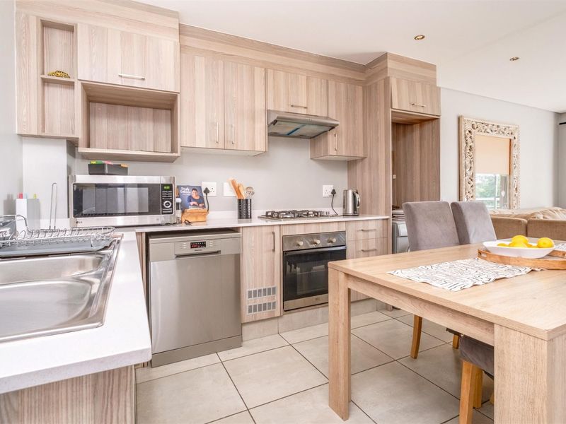 Modern open-plan kitchen featuring light wood cabinetry, stainless steel appliances, gas hob, and tiled flooring, seamlessly flowing into the dining area.