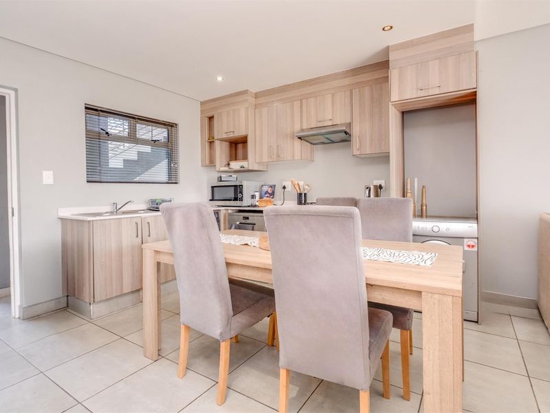 Modern open-plan kitchen and dining area featuring light wood-finish cabinetry, tiled flooring, and integrated appliances in a well-maintained townhouse setting.