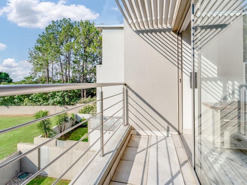 A clean, modern balcony featuring a stainless steel balustrade, tiled flooring, and a slatted pergola, offering views over the garden area.