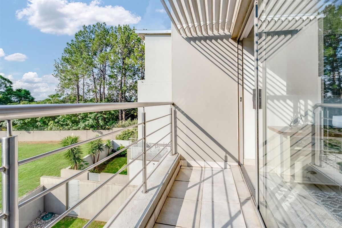 A clean, modern balcony featuring a stainless steel balustrade, tiled flooring, and a slatted pergola, offering views over the garden area.
