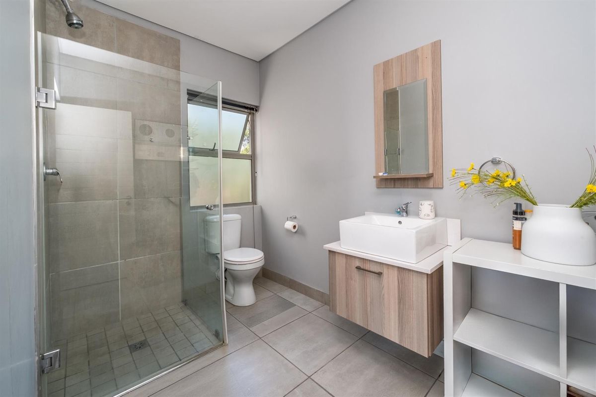 Modern bathroom featuring a glass-enclosed shower, wall-mounted vanity with vessel sink, and neutral floor-to-ceiling tiling.