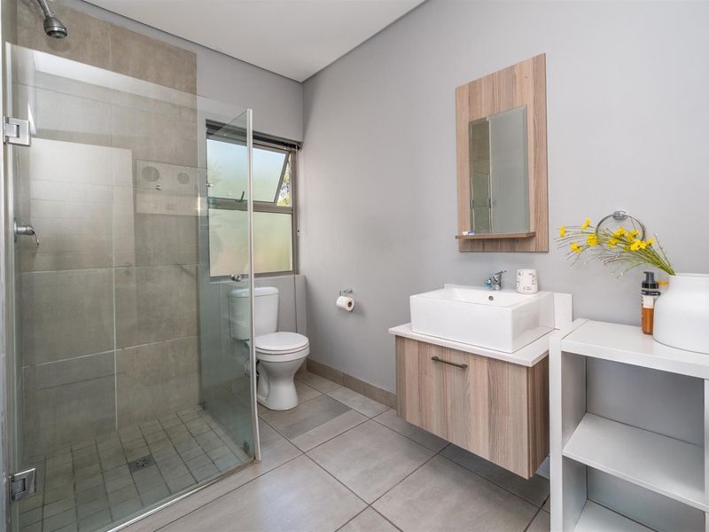 Modern bathroom featuring a glass-enclosed shower, wall-mounted vanity with vessel sink, and neutral floor-to-ceiling tiling.