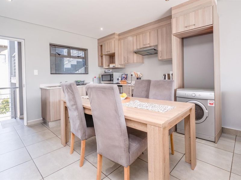 Open-plan kitchen and dining area featuring modern wood-finish cabinetry, tiled flooring, and integrated appliance space with direct access to an outdoor balcony.