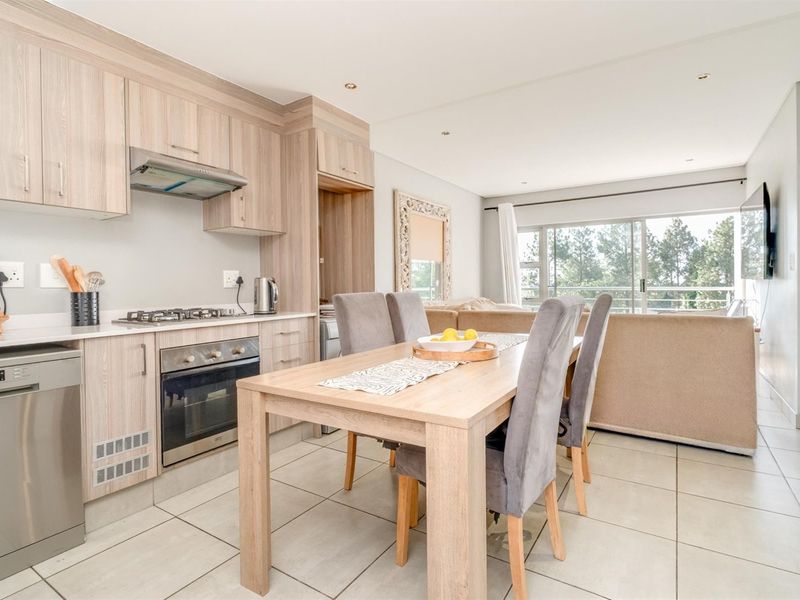 Modern open-plan kitchen and dining area featuring light wood cabinetry, integrated appliances, tiled flooring, and seamless flow to the living space and balcony.