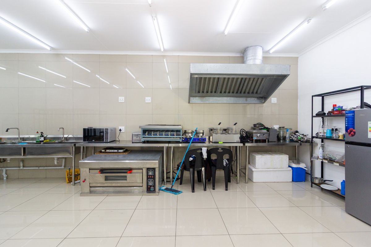A clean, functional commercial kitchen featuring tiled surfaces, stainless steel prep counters, a commercial oven, and an industrial extractor fan.