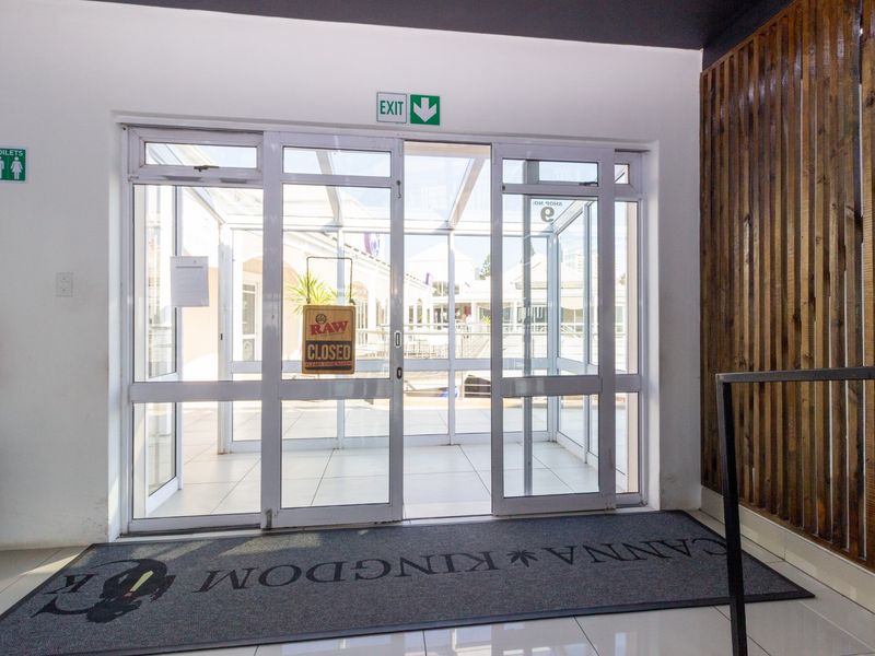 A clean, modern restaurant entrance featuring white tiled floors, aluminium glass sliding doors, and decorative timber slat wall paneling.