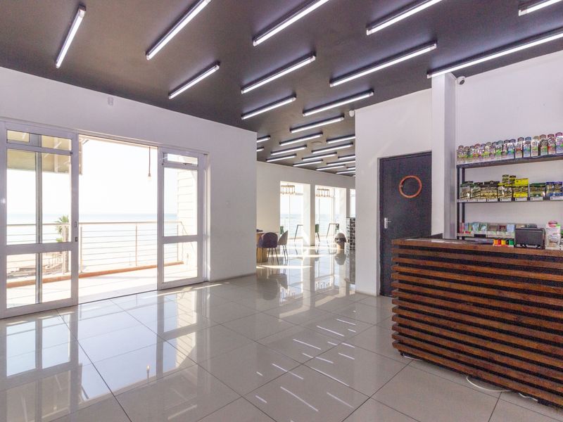 Spacious open-plan restaurant area featuring polished tile flooring, modern linear ceiling lighting, and direct access to an outdoor balcony with sea views.