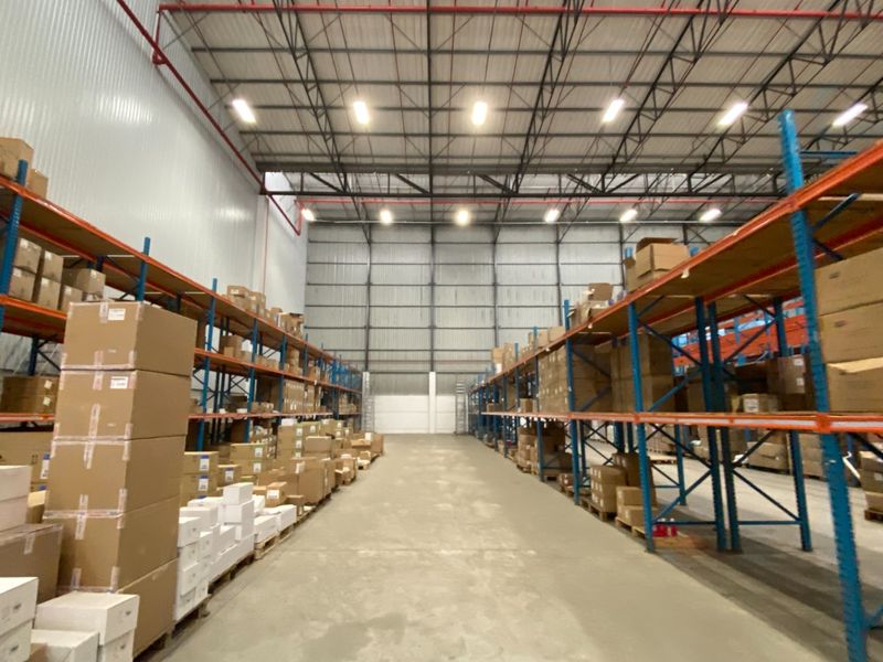 Spacious industrial warehouse featuring high-bay lighting, exposed steel roof trusses, durable concrete flooring, and extensive integrated racking systems for storage.
