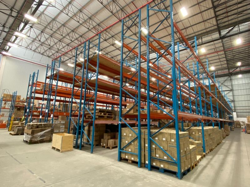 Spacious industrial warehouse featuring high-bay lighting, exposed steel roof trusses, durable concrete flooring, and an extensive multi-level pallet racking system.