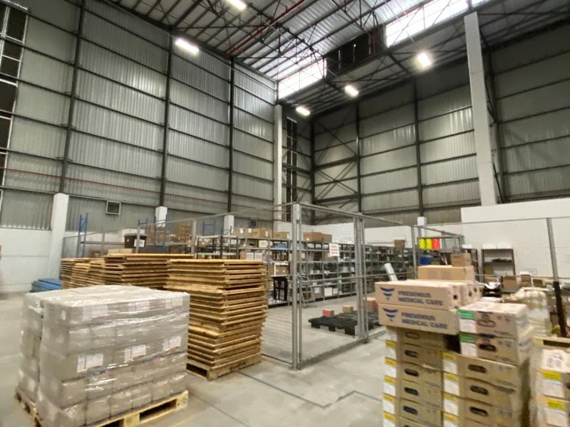 Spacious industrial warehouse area featuring high ceilings, exposed steel structural elements, concrete flooring, and secure wire mesh partitioning for storage organization.